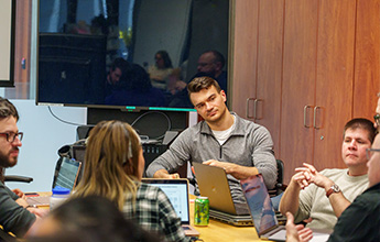 A group of people engaged in discussion around a conference table, with laptops open