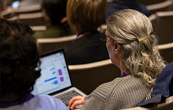 Person seated with a laptop showing graphs during a conference.