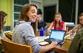 A group of people sitting around a table, with one person in focus, smiling and speaking.
