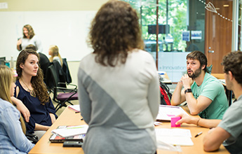 A group of people in a discussion around a table in a bright room with large windows.