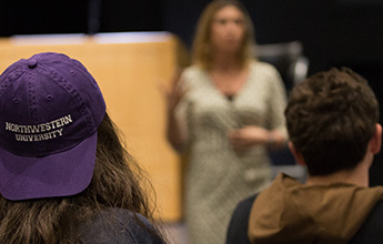 Student wearing a purple cap reading "NORTHWESTERN UNIVERSITY" in a classroom, listening to an instructor.