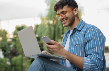 Student sitting outside with an open laptop looking at their phone