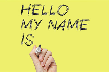 A hand holding a marker writes "HELLO MY NAME IS" on a bright yellow background.