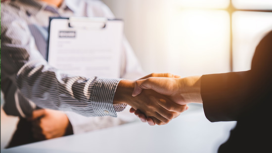 Close-up of a handshake between two people, one holding a clipboard