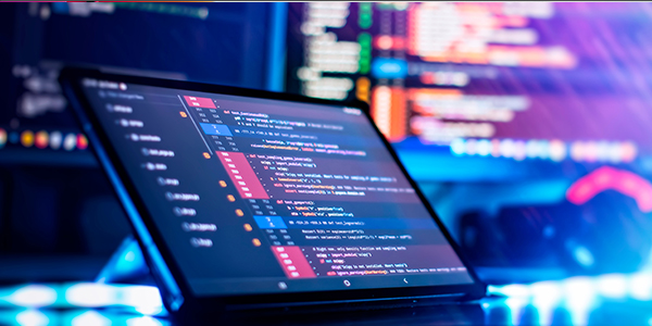 A tablet displaying a code editor with colorful syntax highlighting, set against a background of blurred code on a monitor.